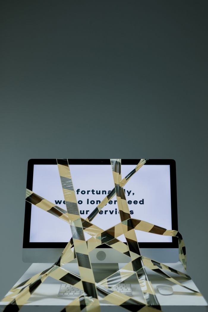 Un écran d’ordinateur affiche un message de fin de contrat avec du ruban de sécurité, illustrant une perte d’emploi.